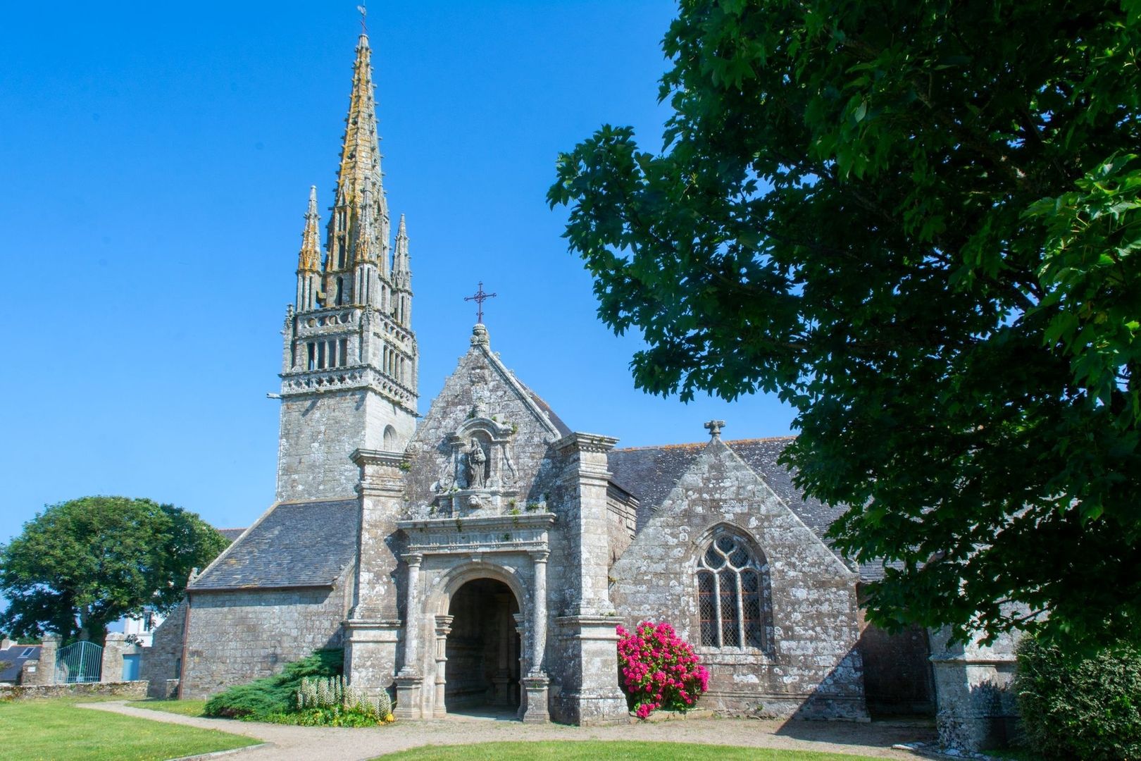 Église bretonne en pierre avec clocher ouvragé sous un ciel bleu